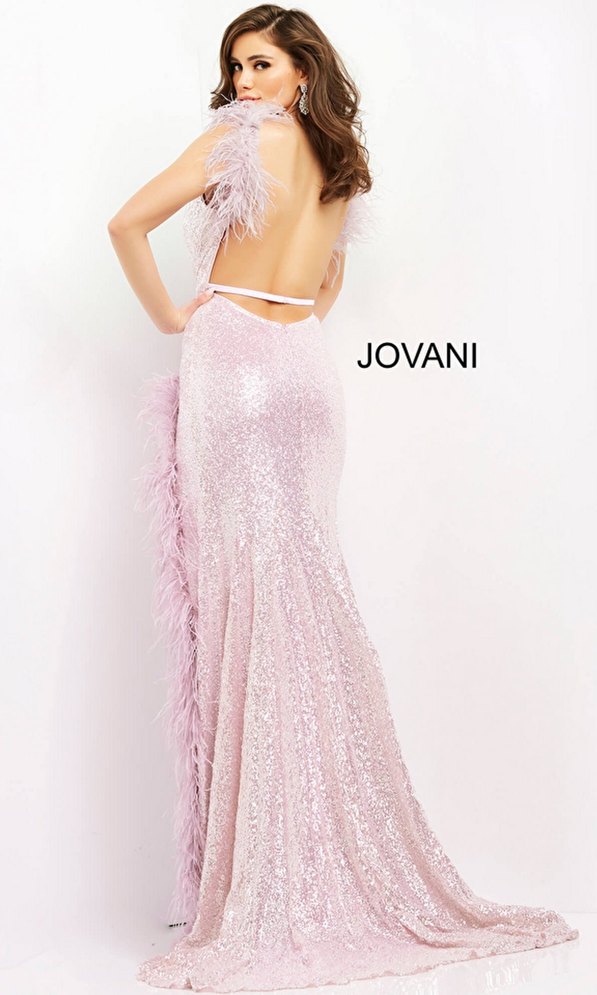 A woman wears the Long Prom Dress 06164 by Jovani, a backless light pink sequin formal gown with feather trim, as she poses against a white background. The word